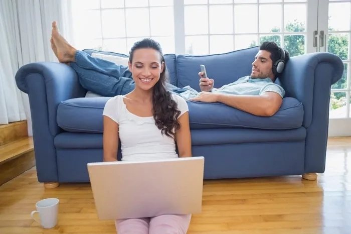 Two people using a laptop and smartphone in a bright living room, illustrating everyday use of a secure, reliable home Wi‑Fi network.